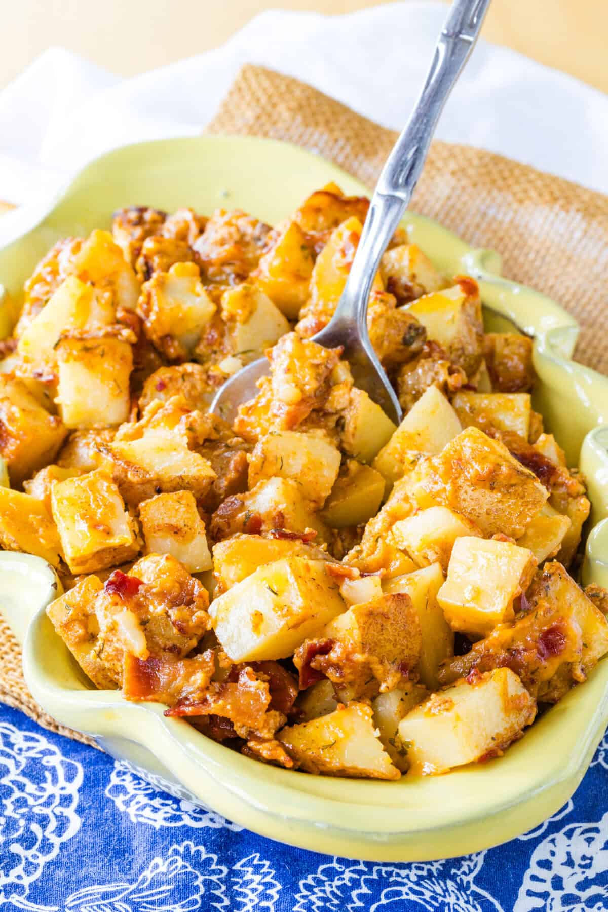 A serving dish of cheesy bacon ranch potatoes with a spoon in it.