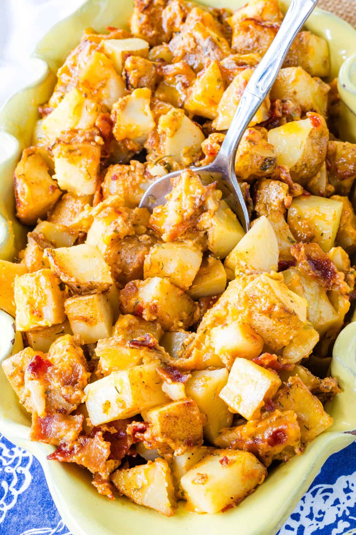 A spoon in an oval-shaped dish of cheesy roasted potatoes.