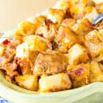 Cubes of roasted potatoes covered in melted cheese and bacon in a serving dish.