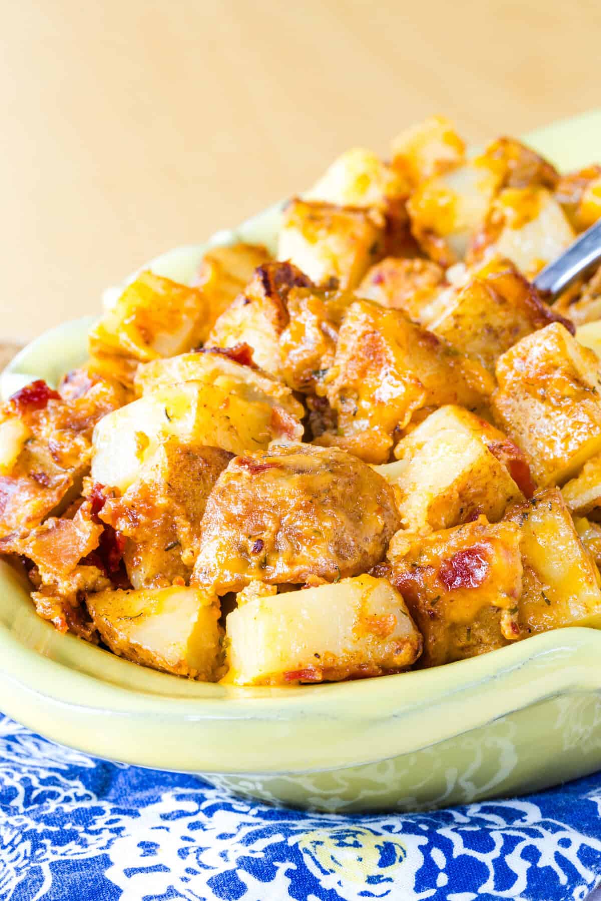 Cubes of roasted potatoes covered in melted cheese and bacon in a serving dish.