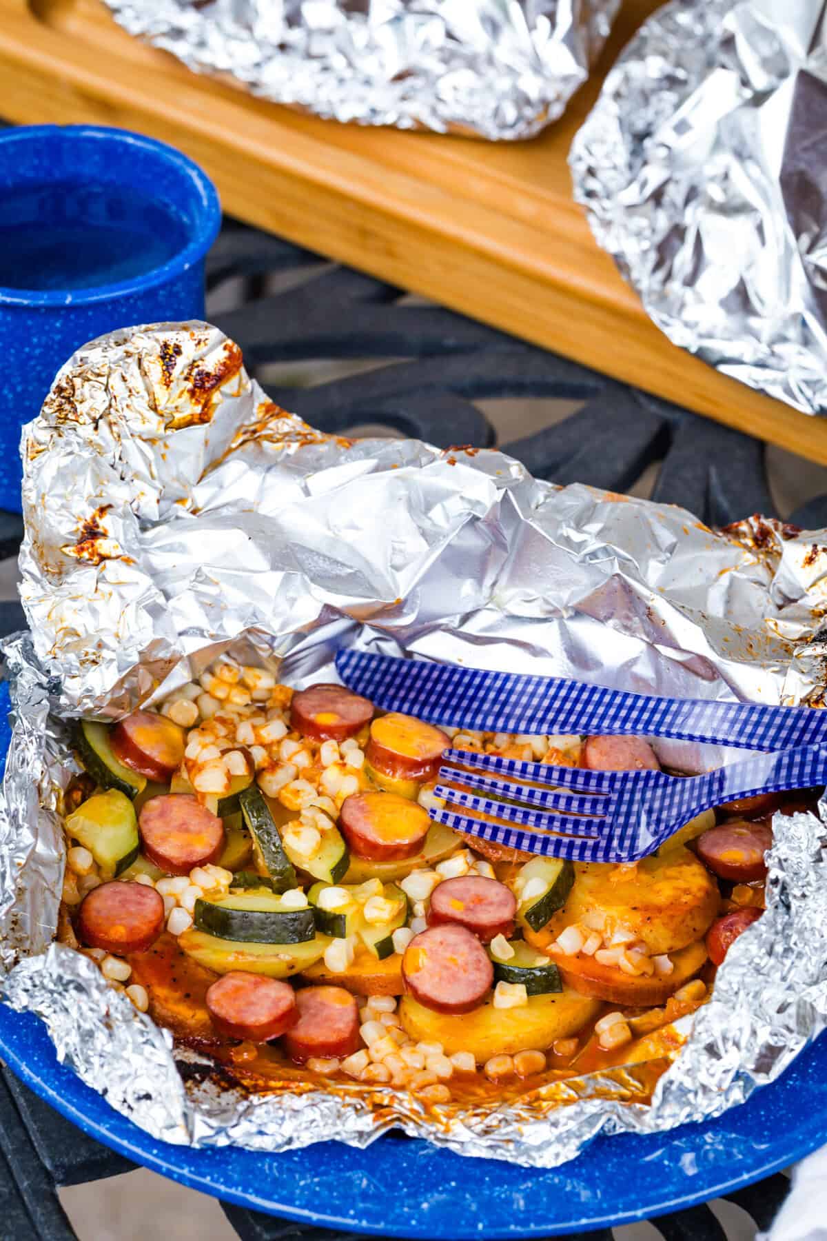 A foil pack dinner with sausage and veggies on a table.