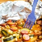 A fork in a sausage foil pack dinner on a blue plate.