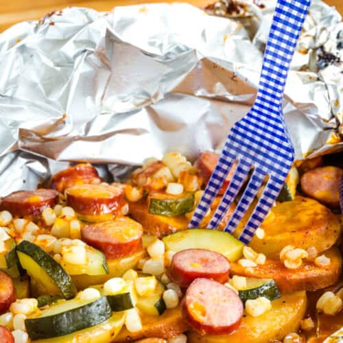 A fork in a sausage foil pack dinner on a blue plate.