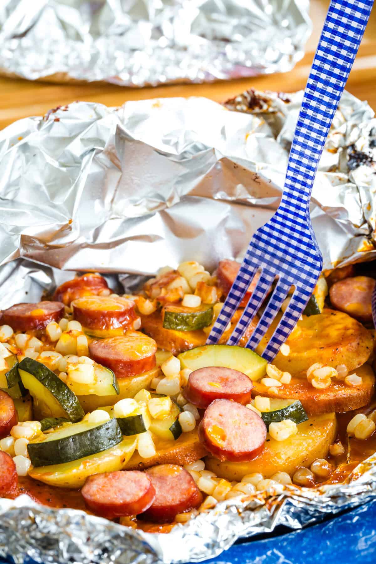 A fork in a sausage foil pack dinner on a blue plate.