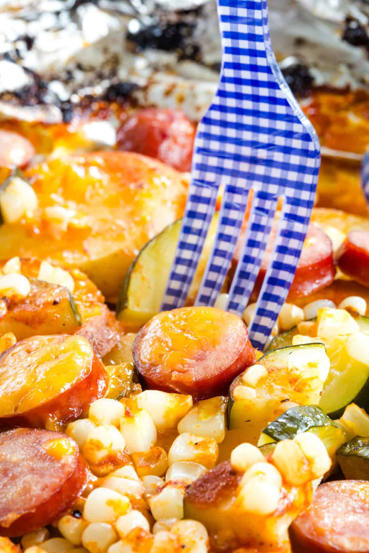 A cloesup of a fork in a mixture of corn, sausage, potatoes, and zucchini.