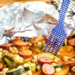 A fork in a foil packet with sausage and veggies with text overlay that says "Cheesy Sausage Foil Pack Dinner".