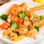 Chicken and vegetable stir fry over rice on a white plate