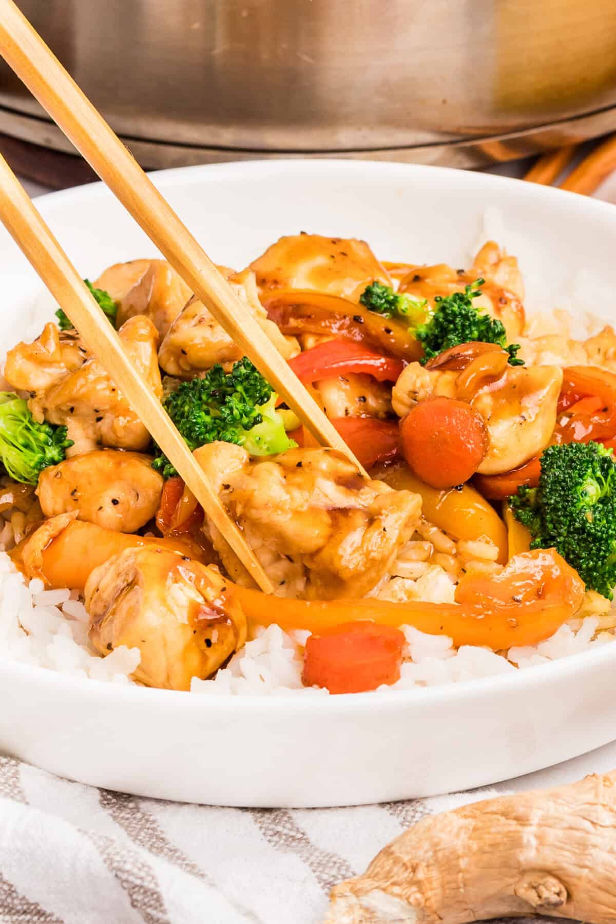 Chopsticks grabbing a piece of chicken from a bowl of chicken and vegetable stir fry
