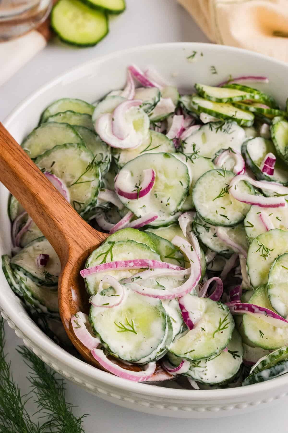 A wooden spoon in a bowl of creamy cucumber salad