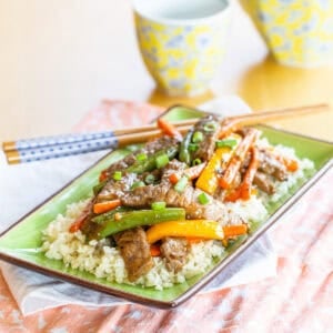 Beef stir fry with vegetables over cauliflower rice on a plate with chopsticks.
