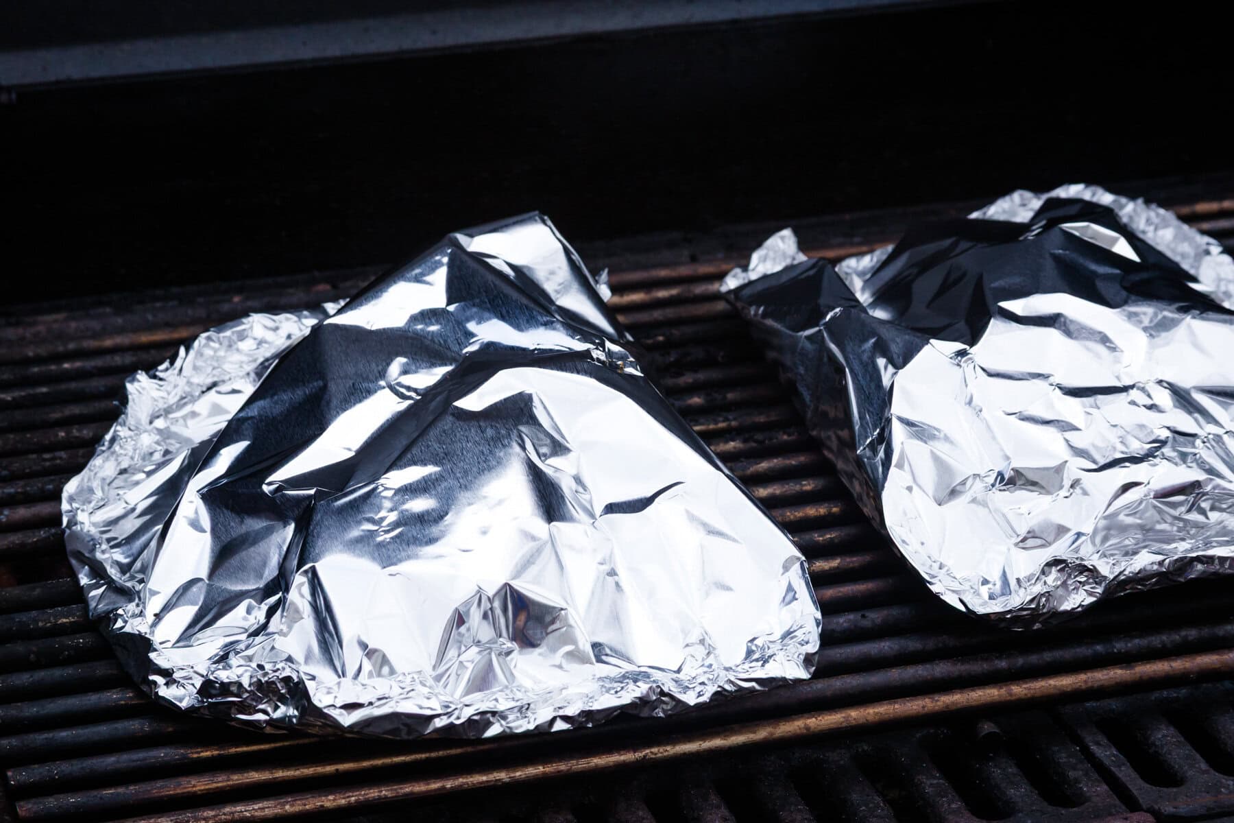 Two foil packets on a grill.