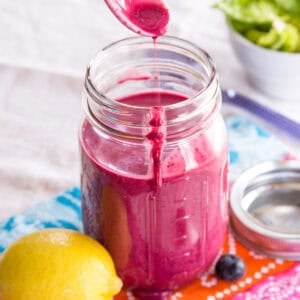 Lemon blueberry chia seed dressing dripping off a spoon into a jar.