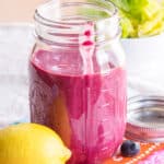 A jar of blueberry chia seed dressing with a lemon and fresh blueberries next to it.