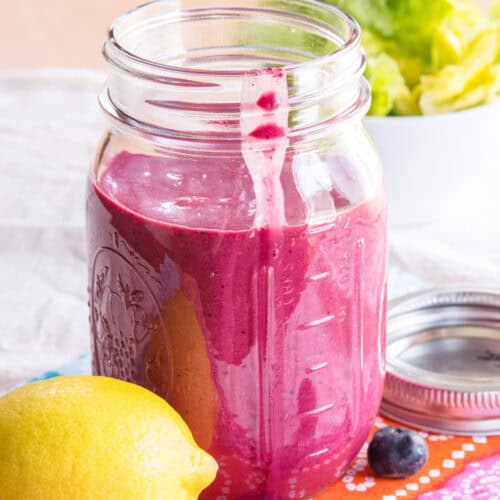 A jar of blueberry chia seed dressing with a lemon and fresh blueberries next to it.