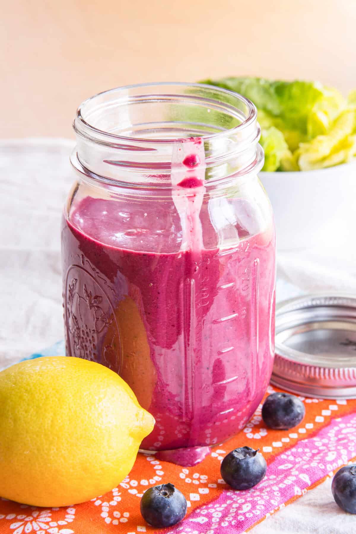 A jar of blueberry chia seed dressing with a lemon and fresh blueberries next to it.