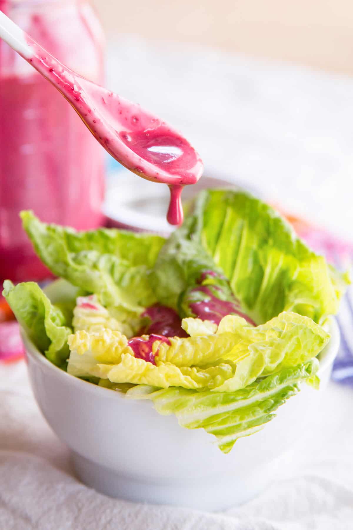 A spoon drizzling blueberry chia seed dressing over a bowl of lettuce.