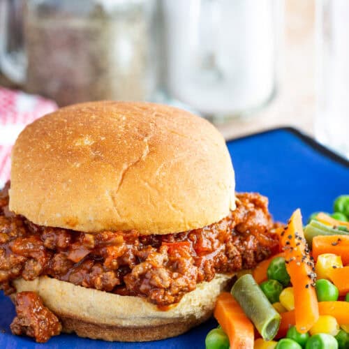 A sloppy joe sandwich on a bun with mixed vegetables on the side.