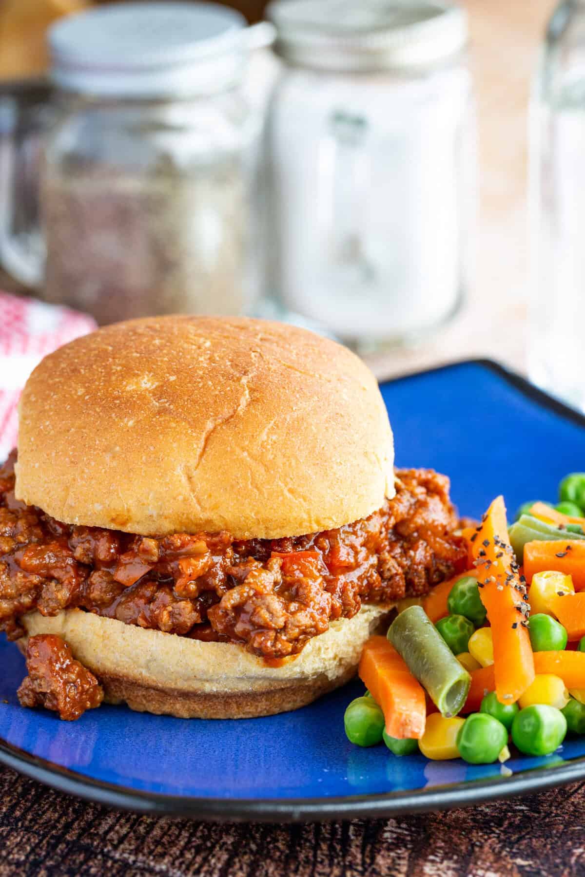 A sloppy joe sandwich on a bun with mixed vegetables on the side.