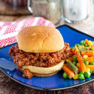 A sloppy joe sandwich on a blue plate with mixed veggies.