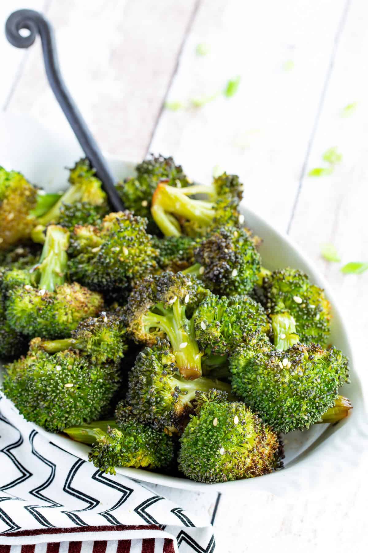 A spoon in a serving dish of maple sesame broccoli.