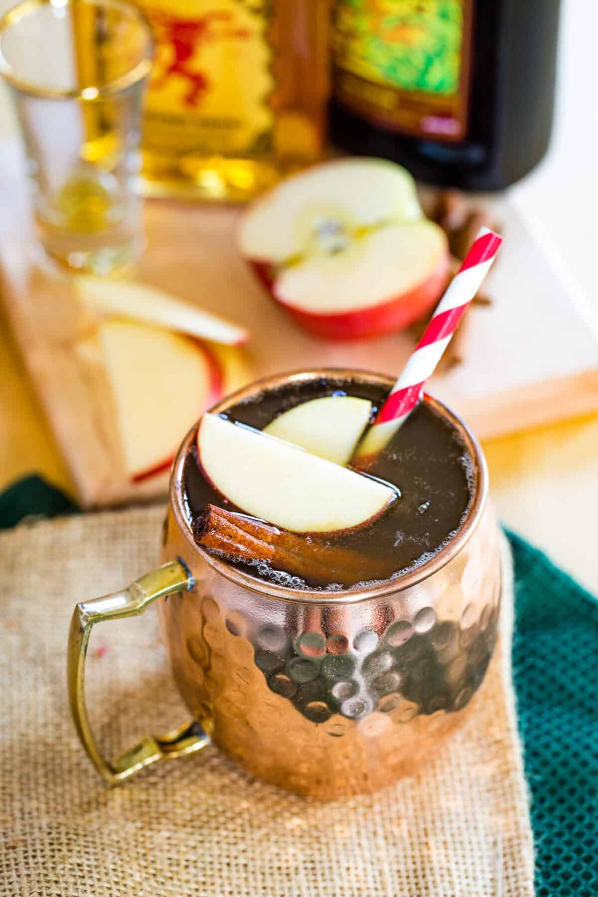 A copper mug with an apple cider mule cocktail with apple sliced floating on top.