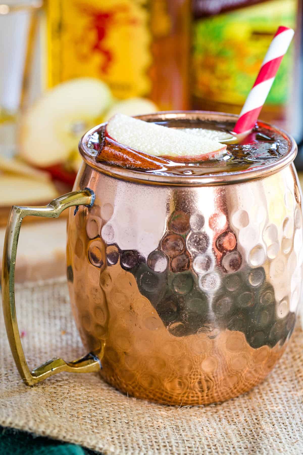 A closeup of a drink in a copper mug with a striped straw.