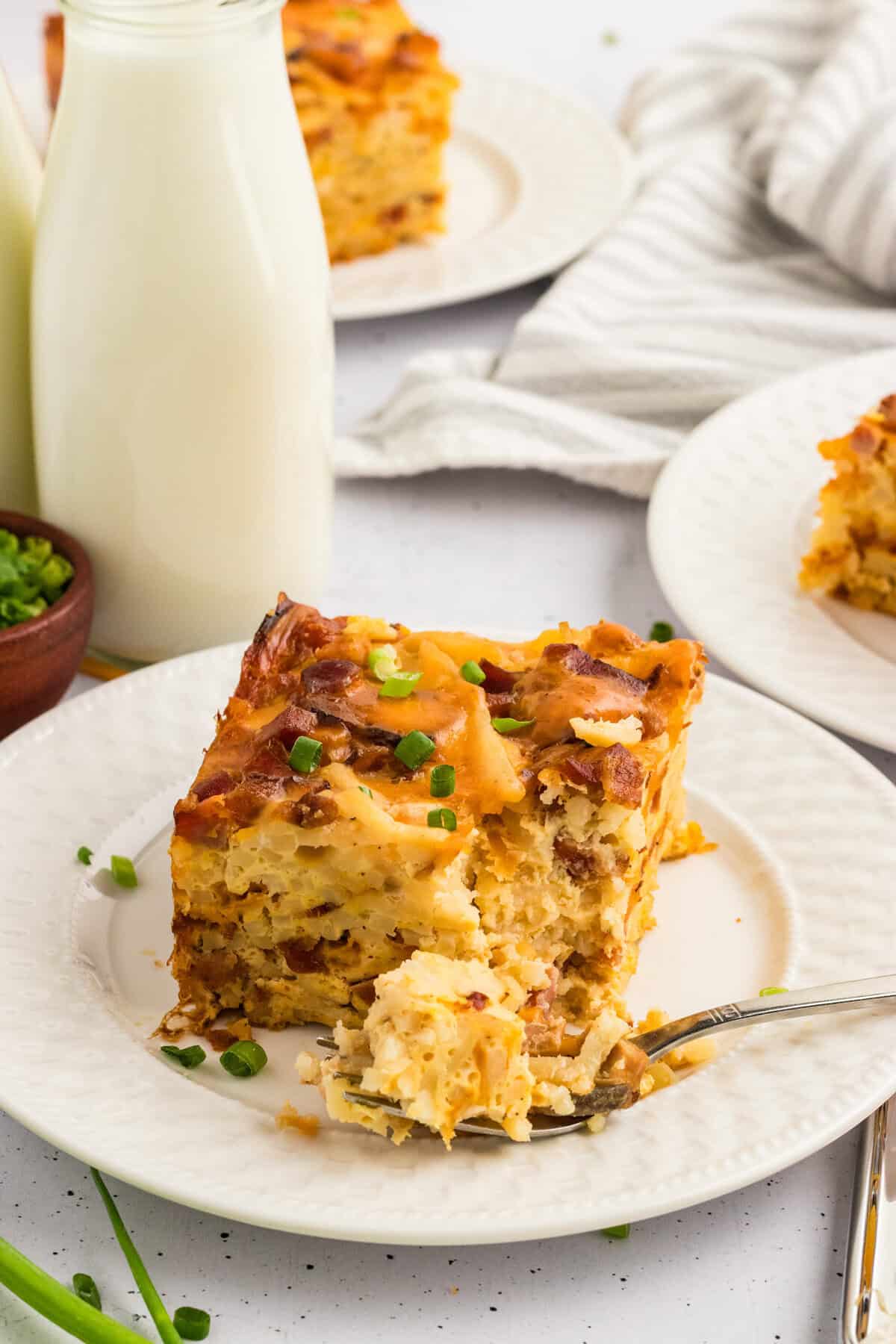 A bite of breakfast casserole on a fork next to a slice of the casserole