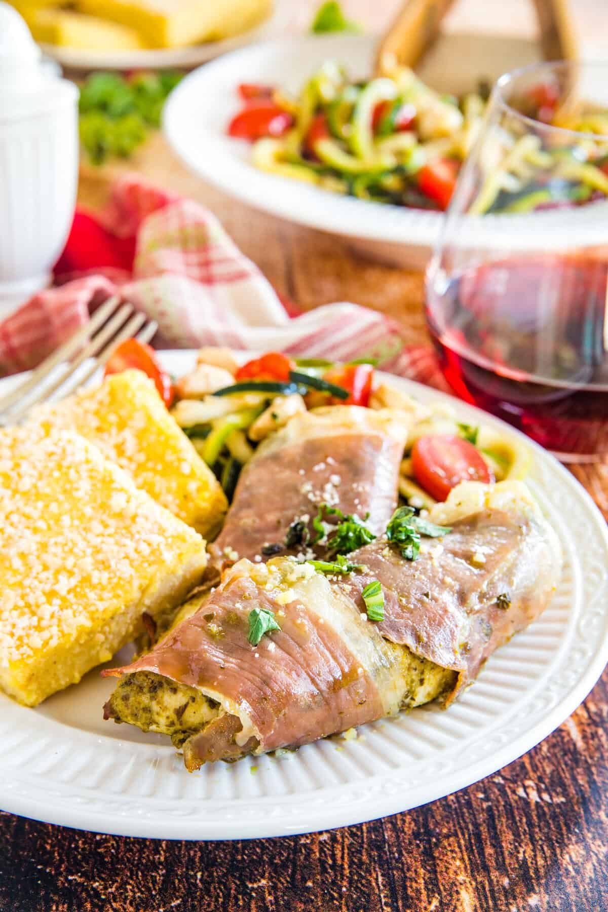 Prosciutto chicken tenders on a white plate with polenta squares.