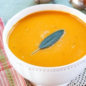 A bowl of cheddar cheese butternut squash soup with a sage leaf on top.