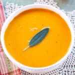 A birdseye view of a bowl of butternut squash soup garnished with a sage leaf.