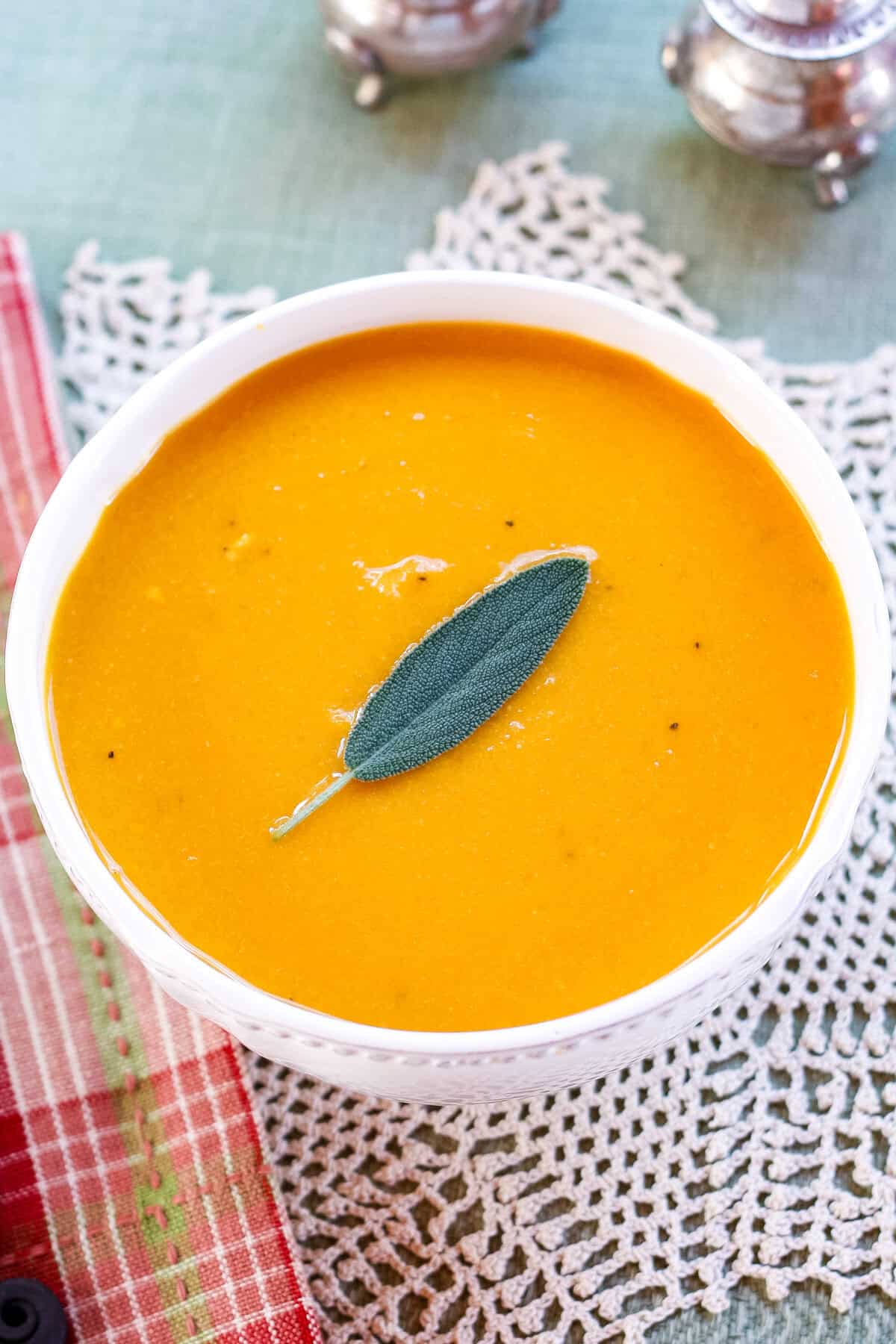 A birdseye view of a bowl of butternut squash soup garnished with a sage leaf.