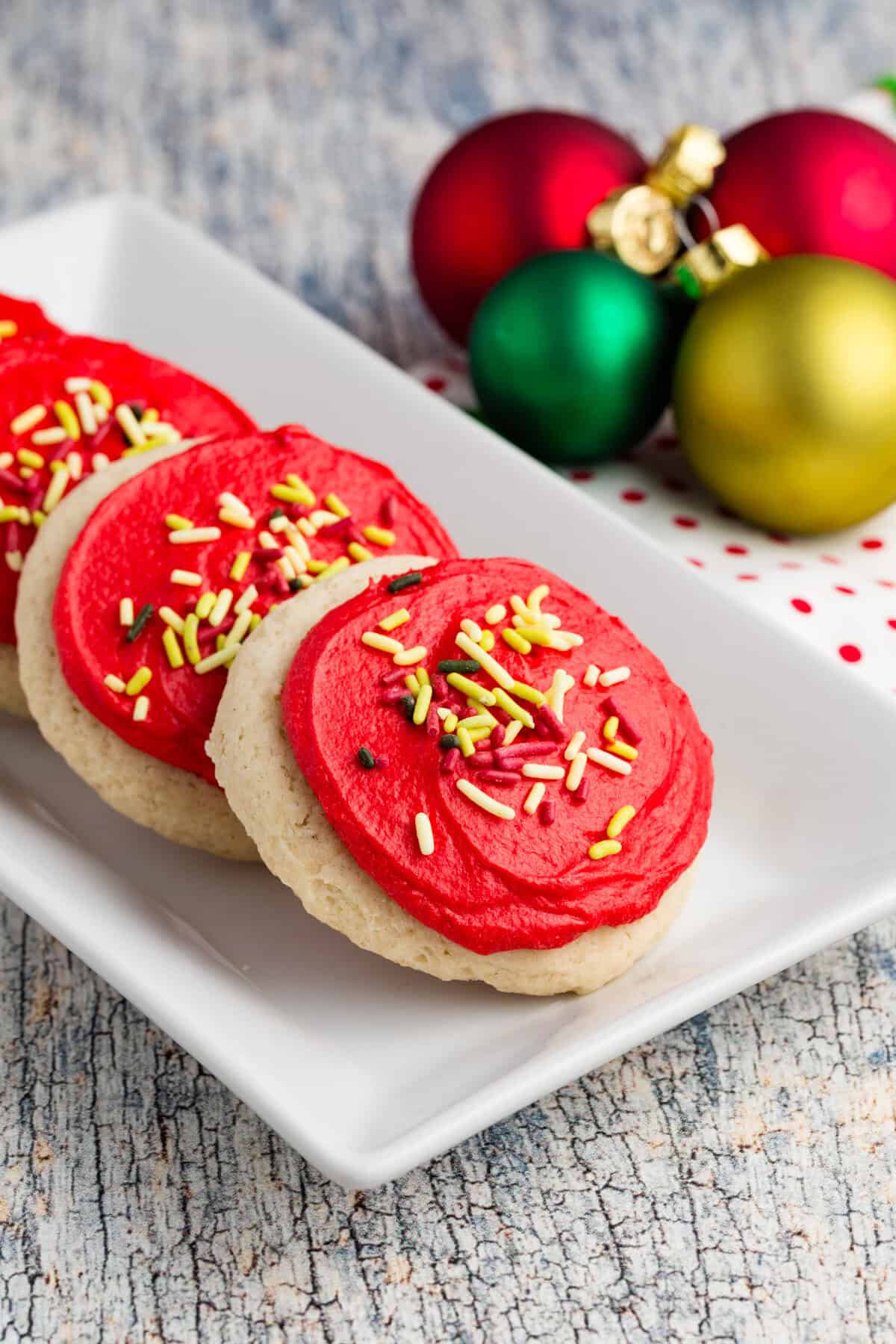 Gluten free Lofthouse cookies with red frosting and Christmas sprinkles on a white platter.