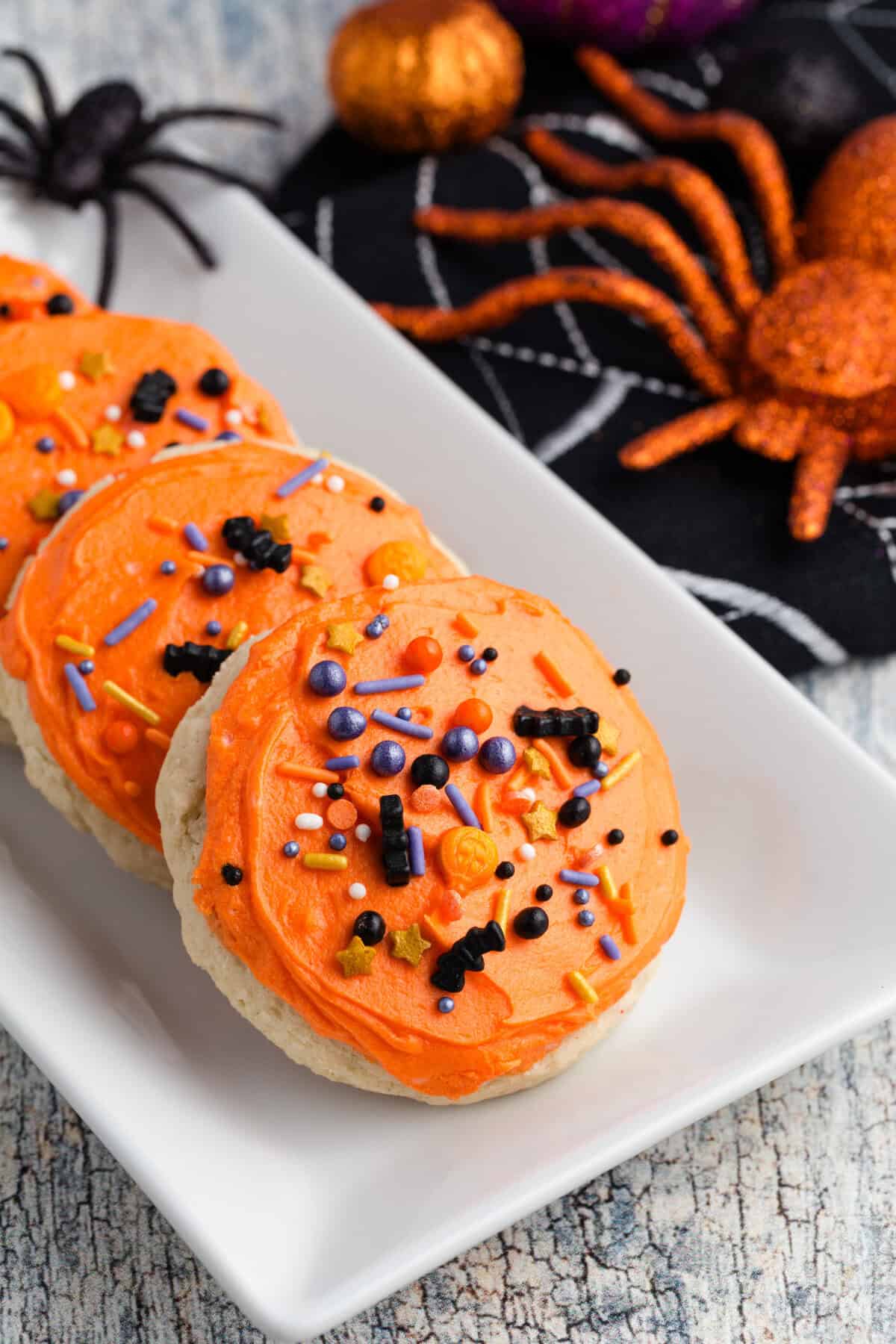 Gluten free Lofthouse cookies with orange frosting and Halloween sprinkles on a white platter.
