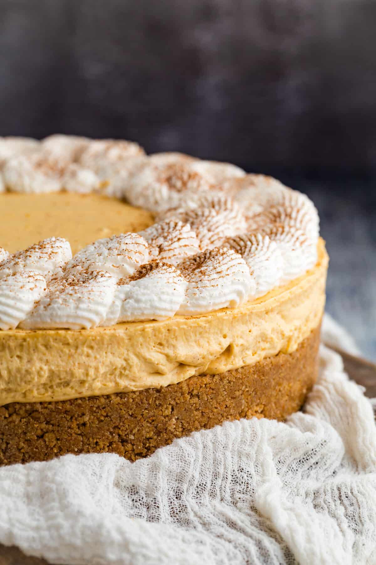 With a graham cracker crust and fluffy pumpkin filling, this gluten free no-bake pumpkin cheesecake is an easy fall dessert. A gluten free no bake pumpkin cheesecake on a kitchen towel