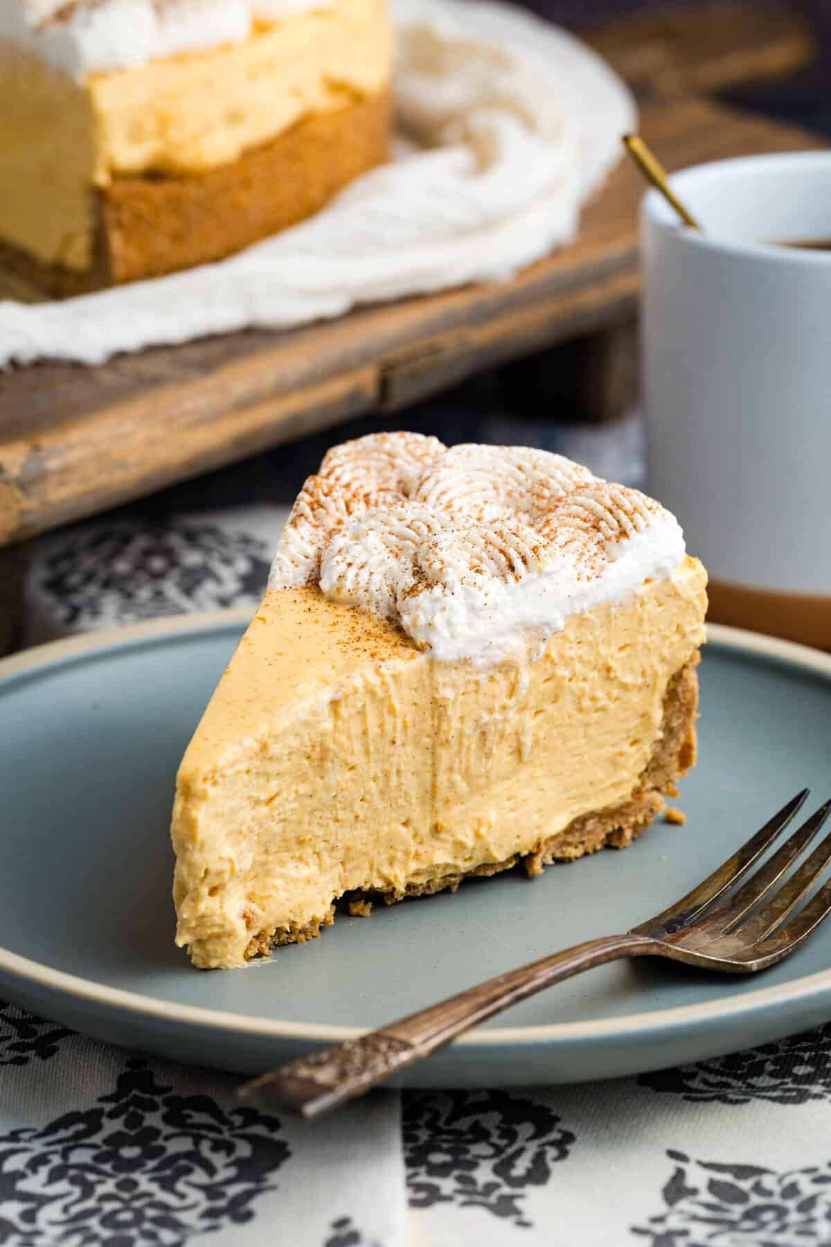 With a graham cracker crust and fluffy pumpkin filling, this gluten free no-bake pumpkin cheesecake is an easy fall dessert. A slice of gluten free no bake pumpkin cheesecake on a blue plate