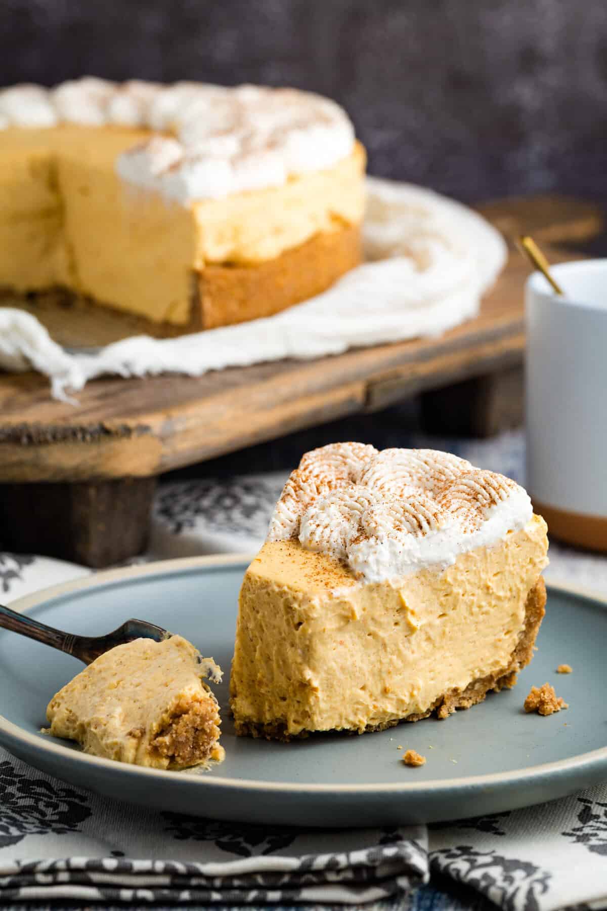 With a graham cracker crust and fluffy pumpkin filling, this gluten free no-bake pumpkin cheesecake is an easy fall dessert. A slice of gluten free no bake pumpkin cheesecake on a plate in front of the cheesecake