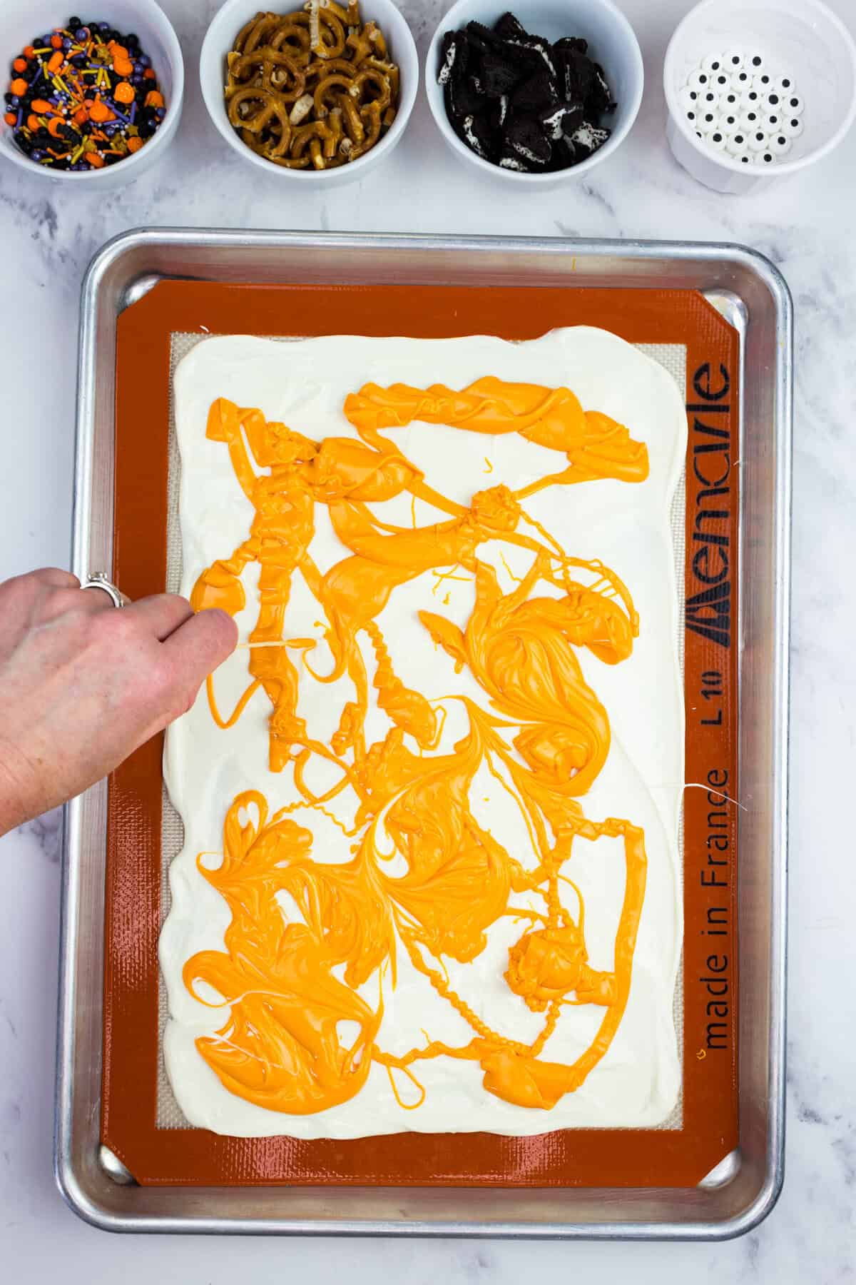 A hand swirling orange chocolate nto white chocolate.
